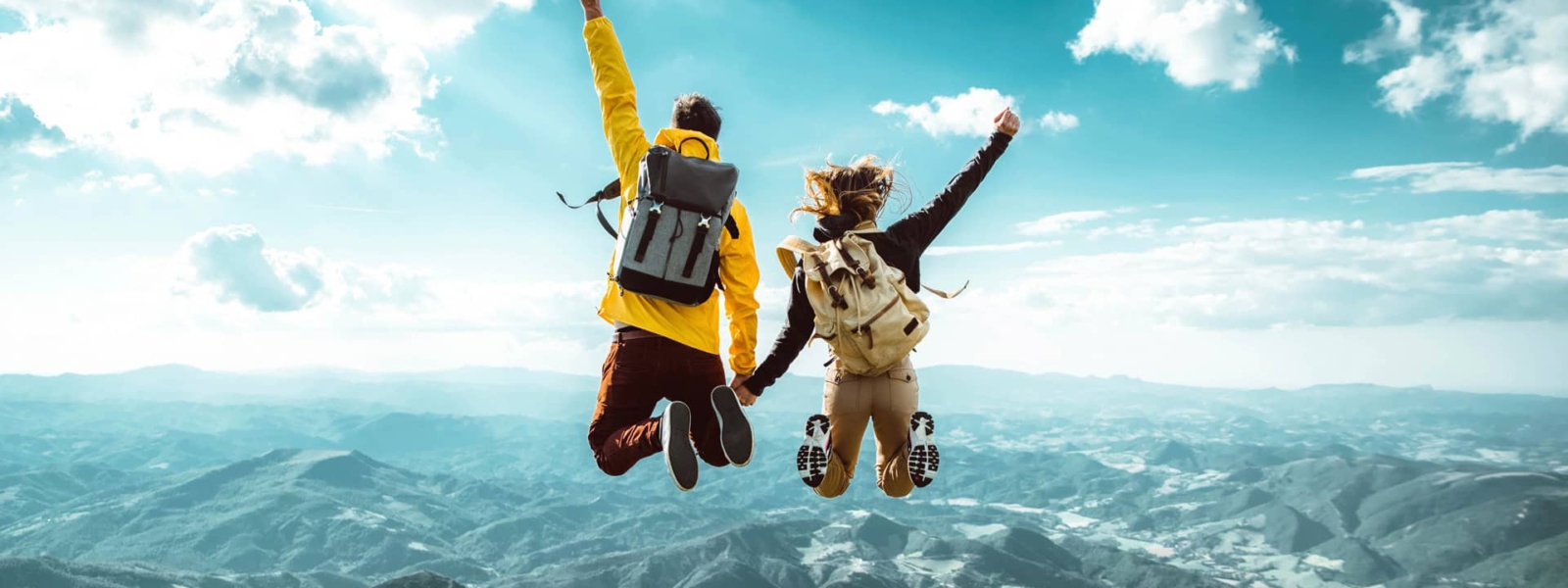 Hikers with backpacks jumping with arms up on top of a mountain.