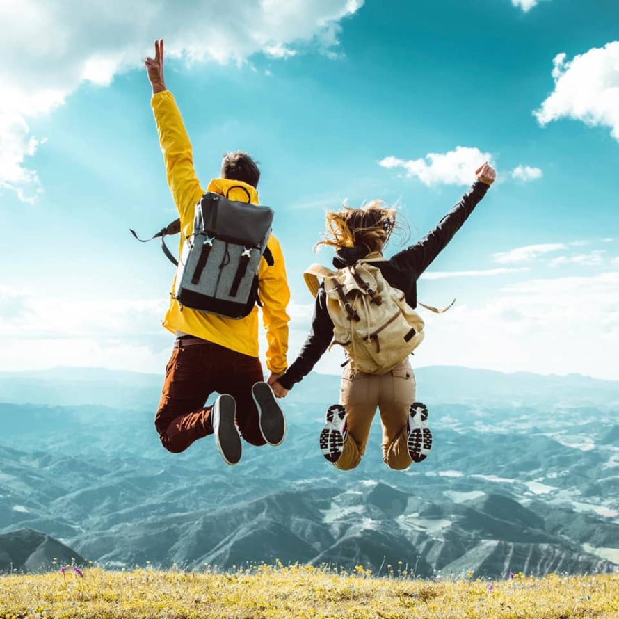 Hikers with backpacks jumping with arms up on top of a mountain.